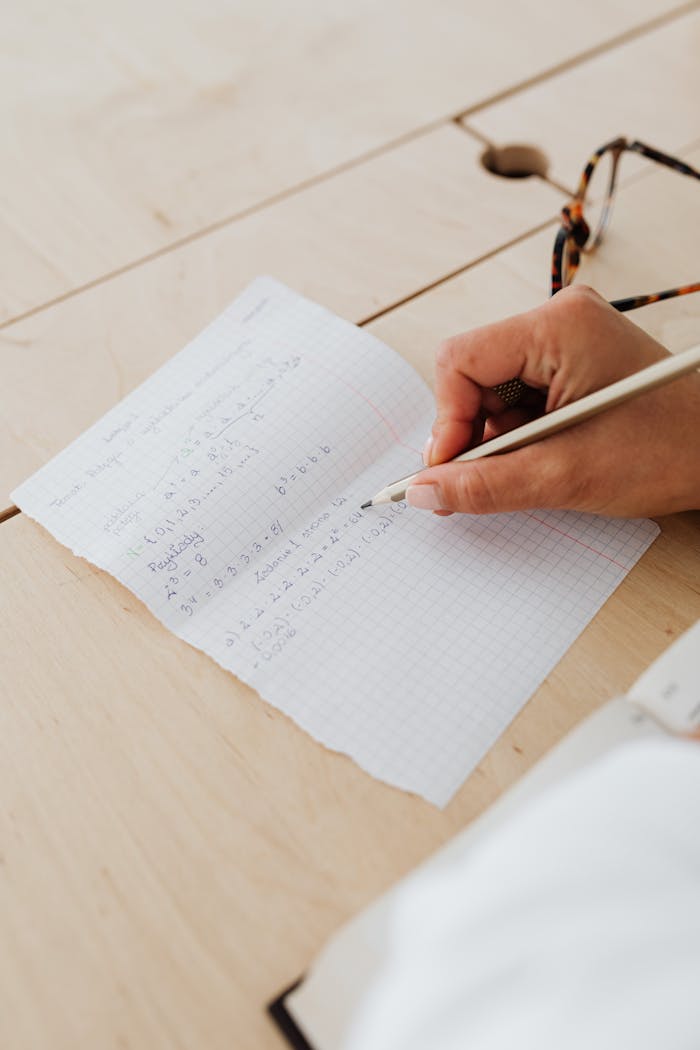 Close-up of hand writing math equations on graph paper, indicating study and learning.